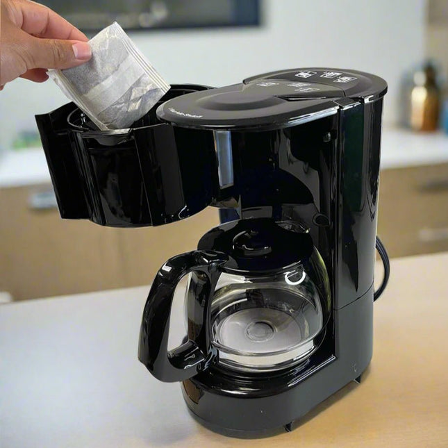 a hand inserting a coffee bag into a black coffee machine