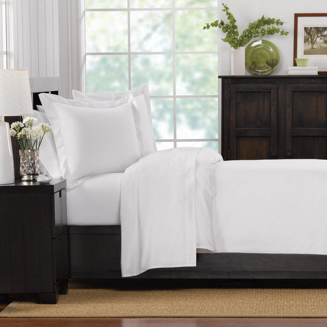 White bedding set on a bed in a bedroom with a window and decor.