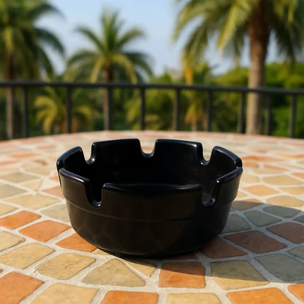 Black ceramic ashtray on a tiled table with palm trees in the background