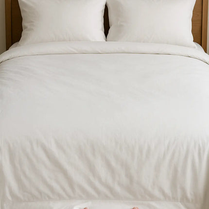 Person holding a white comforter over a neatly made bed with wooden headboard.