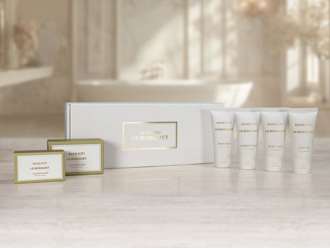 Makari Le Boisquet gift set featuring a white box with gold lettering, two small boxed items, and four white tube containers with gold lettering, arranged on a light marble surface with a softly blurred bathroom background.