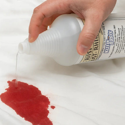 Hand applying a red liquid to a stain on a white surface with a bottle labeled 'Rust-Rhino