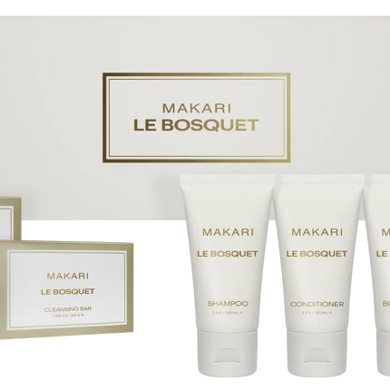Makari Le Bosquet self-care gift set featuring five white toiletry tubes (shampoo, conditioner, body wash, lotion) and three matching boxed items, arranged in front of a large white gift box with gold lettering.