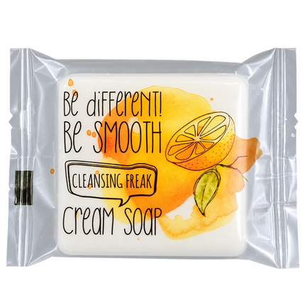 A packaged cream soap bar with a clear plastic wrapper. The soap inside is white, and the wrapper features a watercolor-style yellow and orange citrus graphic with the text 'Be different! Be SMOOTH Cleansing Freak Cream soap'.
