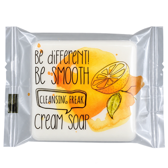 A packaged cream soap bar with a clear plastic wrapper. The soap inside is white, and the wrapper features a watercolor-style yellow and orange citrus graphic with the text 'Be different! Be SMOOTH Cleansing Freak Cream soap'.