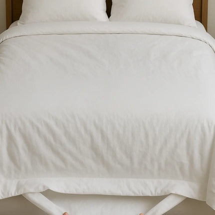 Person holding white duvet over a neatly made bed with wooden headboard.